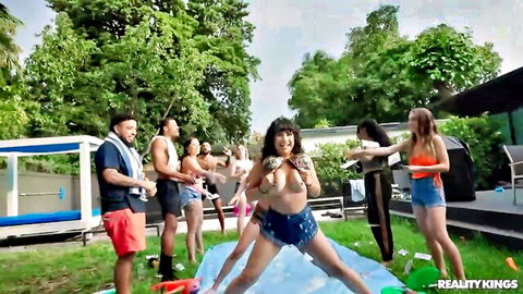 Topless brunette MILF squeezes her big tits outdoors on blue slip n slide at Reality Kings party