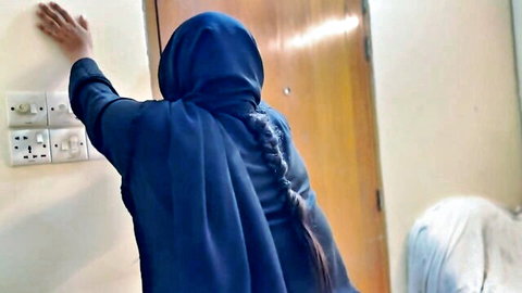 Arabian step-mom in blue hijab leaning against wall, teasing pose