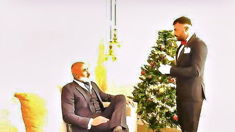 Muscular suited hunk stands by Christmas tree as bald daddy in gray vest sits seductively for gay Xmas tease