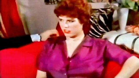Busty redhead with huge natural tits spilling from open purple blouse on couch with man behind her