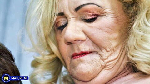 Close-up of mature blonde granny with wrinkled face, heavy makeup and plump red lips looking aroused