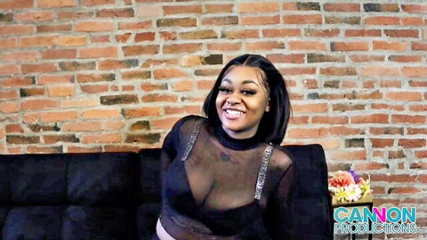 Tenikaa smiling in sheer black top, showcasing curves and cleavage