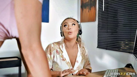 Blonde British babe in open blouse with headphones looks surprised at desk