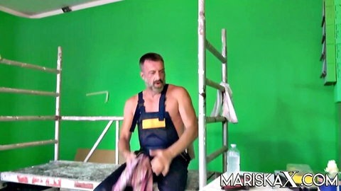 Shirtless muscular man in blue overalls holding pink lingerie in green screen studio