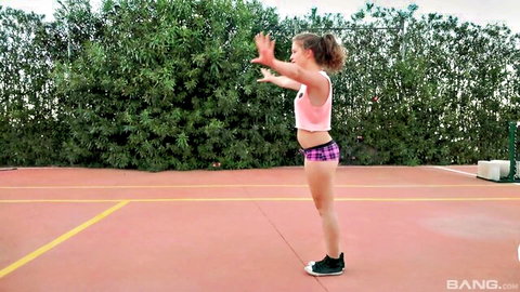 Sexy teen girl in tight pink shorts and crop top posing arms up on outdoor tennis court