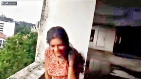 Sexy Indian woman in colorful printed dress posing on outdoor balcony with city view