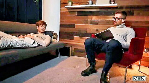 Handsome ginger twink lounging on couch as glasses guy reads book in cozy room