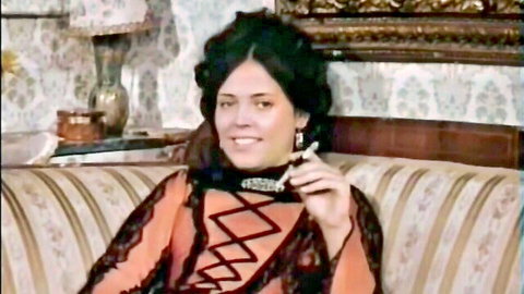 Vintage brunette with big tits in sexy orange lace dress smoking cigarette on couch