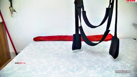 Black BDSM sex swing harness hanging over white bed with red sheet for rough kinky fucking