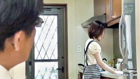 Japanese housewife in apron and suspenders washing dishes at sink while man watches from behind