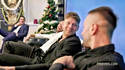 Group of suited men laughing on couch in Christmas room with tree.