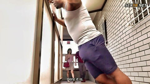 Muscular ebony hunk in tight purple shorts leans on balcony railing with petite Asian woman in pink dress inside