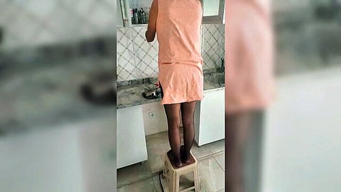 Mature woman in short orange dress and black pantyhose standing on stool teasing upskirt ass in bathroom