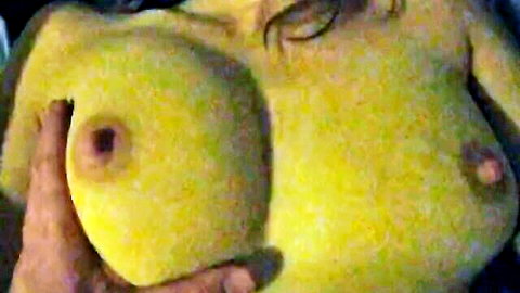 Hands squeezing massive yellow-painted big tits with erect nipples