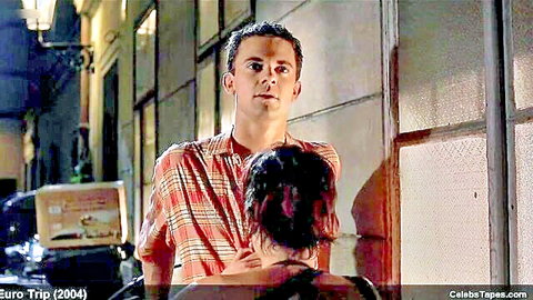 Handsome guy in open plaid shirt embraces curly-haired woman from behind in steamy night alley