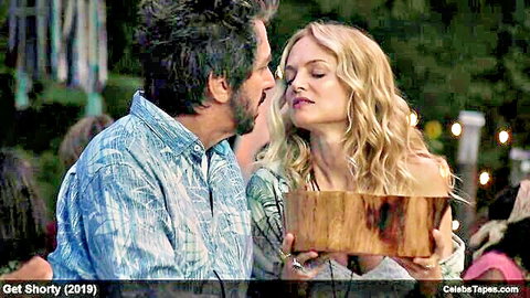 Blonde woman passionately kissed on cheek by bearded man holding wooden plaque outdoors