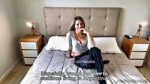 Blonde Latina teen in sweater sitting on bed smiling teasingly in Argentinian casting interview