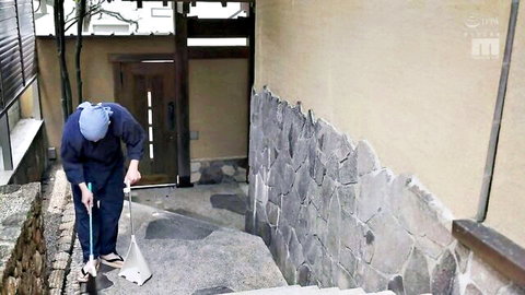 Elegant Japanese innkeeper in blue uniform sweeping ryokan steps