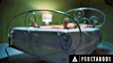 Seductive young woman lying nude in green-lit bed with feet exposed in taboo scene