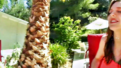 Ecstatic brunette moaning with wet glistening body in red bikini by poolside palm tree