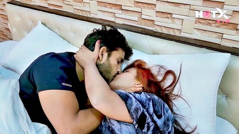 Muscular Indian man passionately kissing redhead woman on bed grabbing her neck