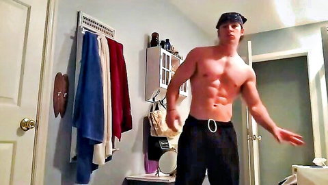 Muscular shirtless young hunk flexing abs in bathroom wearing black pants and bandana