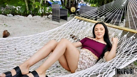 Brunette Latina relaxes in hammock on beach, showing legs in short floral skirt