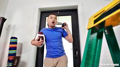 Surprised young guy in blue shirt and khakis holding football peeking through door