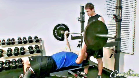 Muscular gay gym bros spotting intense bench press workout in tight shorts