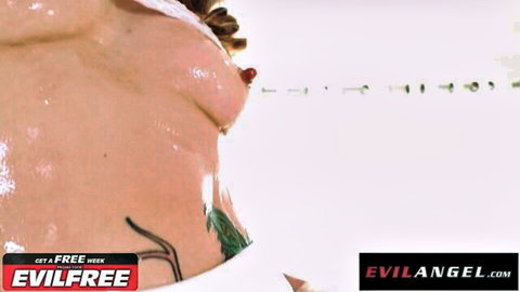 Closeup of shiny oiled tits with pierced nipple and tattoos on glossy skin