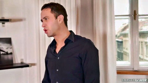 Handsome man in unbuttoned dark shirt standing by window in BUSTY LOVER scene