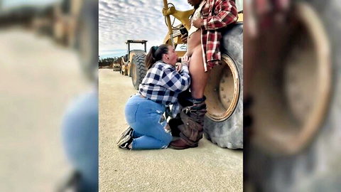 Curvy woman in plaid shirt kneels intimately by John Deere tractor tire outdoors