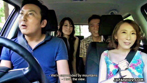 Two smiling Japanese women and two men in car enjoying mountain view on outdoor drive