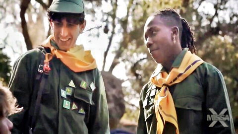 Two young scouts in green uniforms and yellow neckerchiefs in forest, one smiling