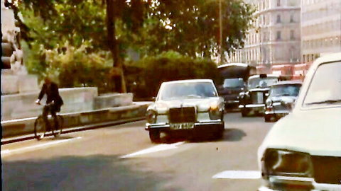 Vintage 1970s European street scene with classic Mercedes car cyclist and traffic.