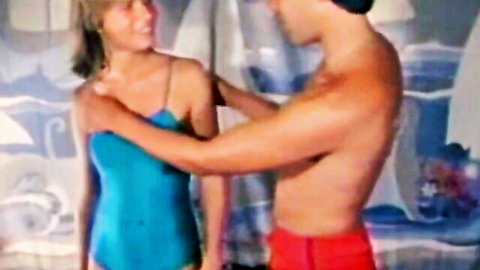 Blonde woman in blue swimsuit and shirtless man in red trunks sharing intimate touch in retro Private Lessons scene