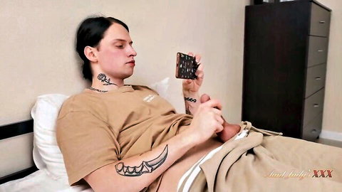 Tattooed guy with neck tats strokes his hard cock while holding phone on bed