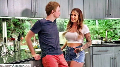 Busty tattooed MILF with huge tits in tiny daisy duke shorts flirts with redhead stud in kitchen