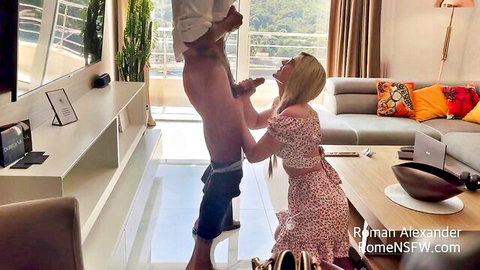 Blonde in floral dress kneels sucking thick cock of standing shirtless man in luxury apartment