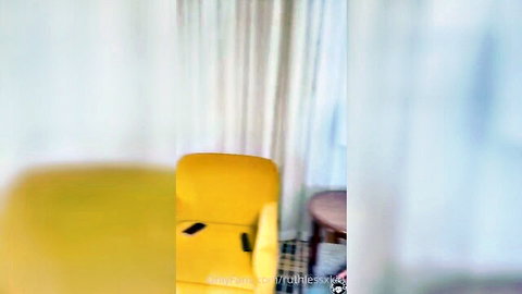Blurry indoor scene of yellow chair with phone near curtained window
