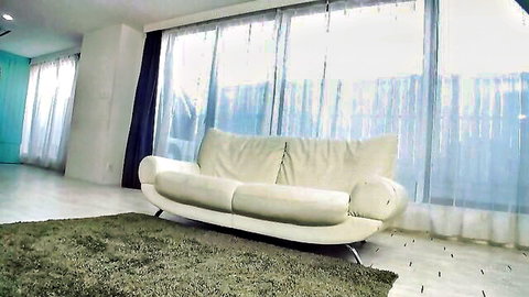 Modern empty living room featuring stylish white curved sofa and large curtained windows.