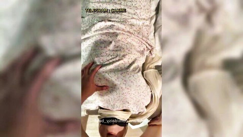 Blindfolded Asian woman in pink floral sheets, hand teasing chest