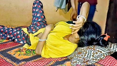 Indian newlywed wife in yellow top and pants lying intimately with husband on bed
