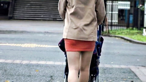 Skinny Asian woman in short red miniskirt and beige coat pushes blue stroller outdoors teasing upskirt view