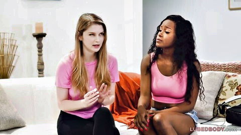 Bunny Colby and Jezabel Vessir in pink outfits chatting on couch, massage fantasy tease