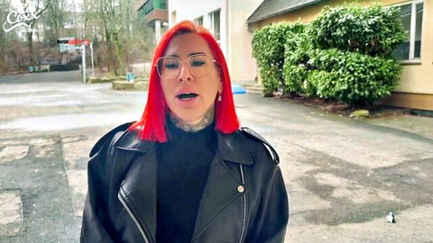 Redhead tattooed woman in glasses and leather jacket talking outdoors