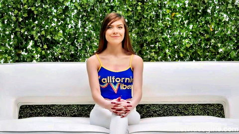 Brunette teen smiling in tight yellow California Vibes tank top and white pants on white couch