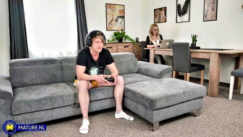Rick Palmer gaming on sofa as mature woman watches from desk