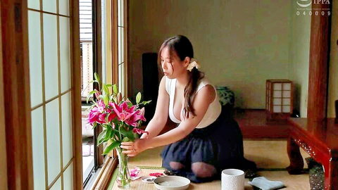 Shiori Tsukada kneeling with pink lilies, busty Japanese beauty in low-cut top showing cleavage