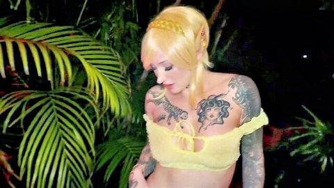 Tattooed blonde Zelda cosplay princess with big tits cleavage in yellow top outdoors